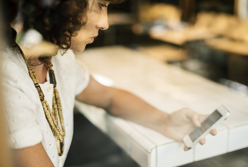 Woman with curly hair using smartphone at cafe counter