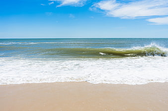 Ocean waves crashing on sandy beach under blue sky
