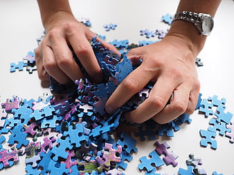 Hands Sorting Blue Jigsaw Puzzle Pieces on White Table