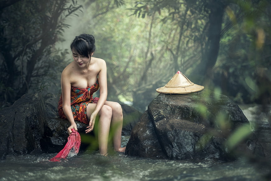 Asian woman in traditional dress washing clothes in a misty forest stream