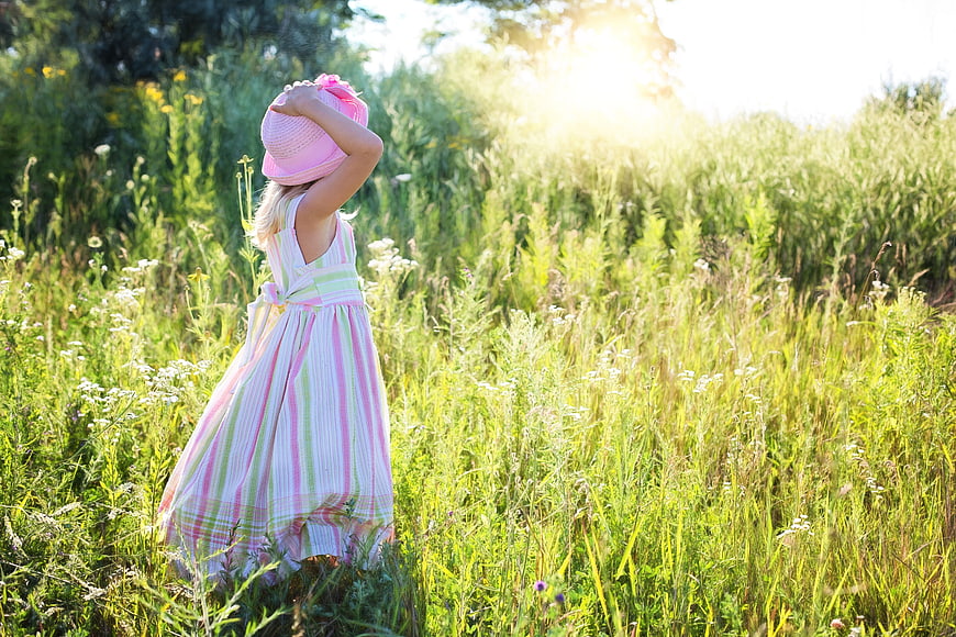 Little Girl in Pink Dress Standing in Sunlit Meadow