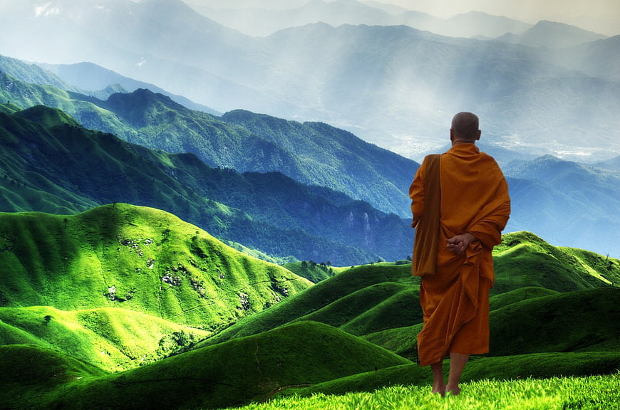 Buddhist Monk Standing on Green Mountain Ridge Overlooking Valley
