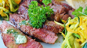Sliced medium-rare steak with herb butter and zucchini ribbons