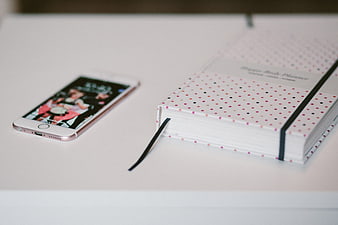 Rose Gold Smartphone and Polka Dot Planner on White Desk