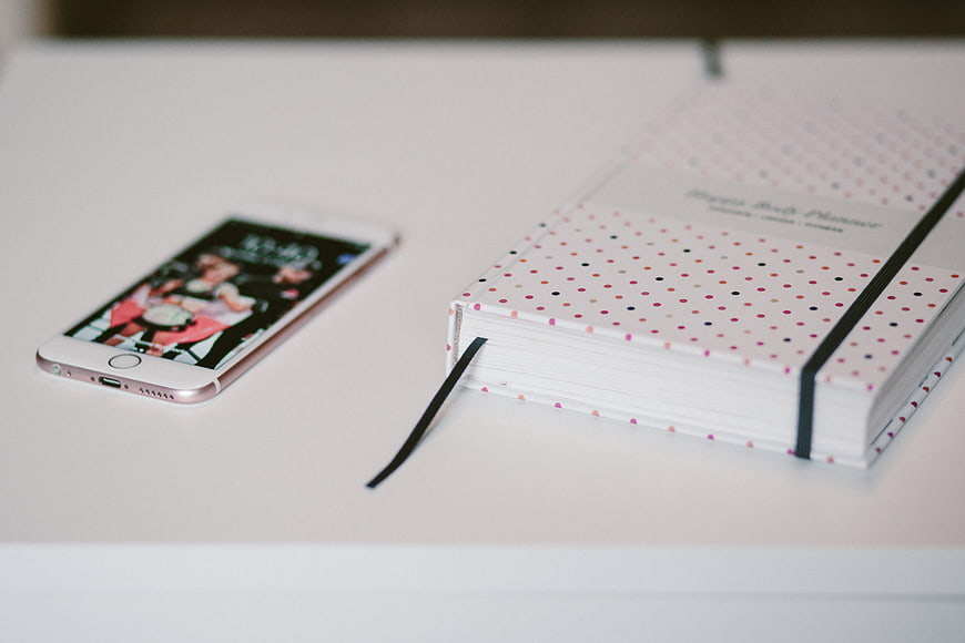 Rose Gold Smartphone and Polka Dot Planner on White Desk