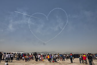 Air show crowd watching heart-shaped smoke trail in sky
