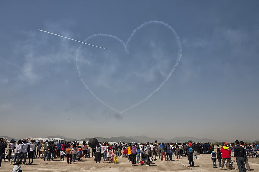 Air show crowd watching heart-shaped smoke trail in sky