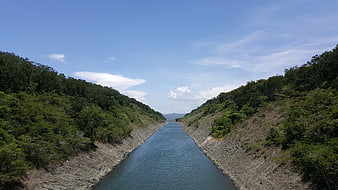 Man-made canal cutting through green hills under blue sky