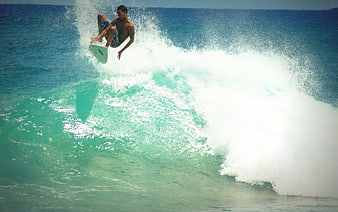Surfer performing aerial maneuver on turquoise ocean wave
