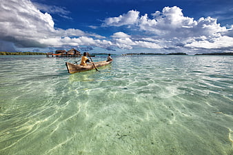 Two people paddling a dugout canoe in clear turquoise lagoon water