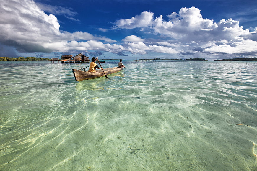 Two people paddling a dugout canoe in clear turquoise lagoon water