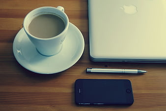 Flat lay of coffee cup, laptop, smartphone, and pen on wooden desk