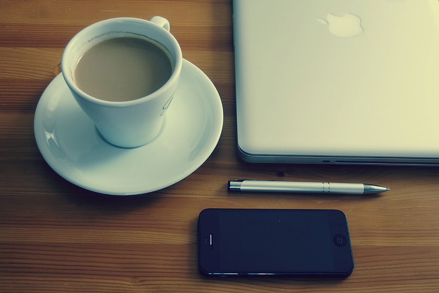 Flat lay of coffee cup, laptop, smartphone, and pen on wooden desk