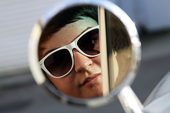 Woman with white sunglasses reflected in car side mirror