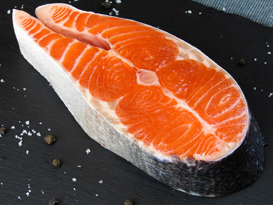 Fresh raw salmon steak on black slate with salt and pepper