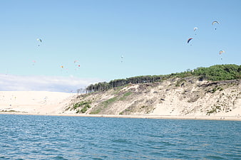 Paragliders soaring over coastal dunes and blue ocean water