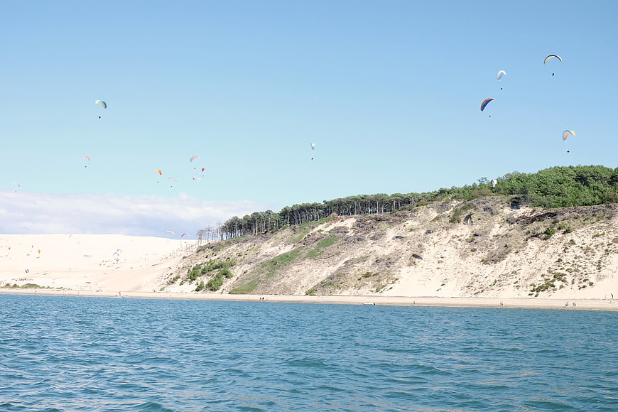 Paragliders soaring over coastal dunes and blue ocean water