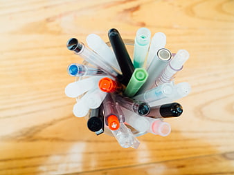 Top View of Colorful Pens in a Glass Cup on Wooden Desk