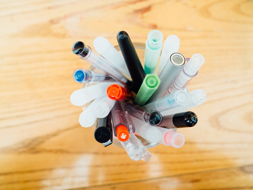 Top View of Colorful Pens in a Glass Cup on Wooden Desk