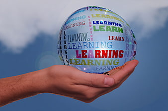 Hand holding transparent bubble with colorful learning text against blue sky
