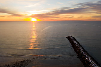 Serene Ocean Sunset with Rocky Jetty and Golden Sky