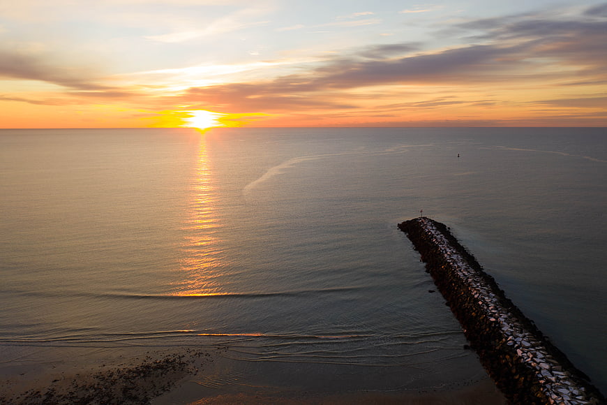 Serene Ocean Sunset with Rocky Jetty and Golden Sky