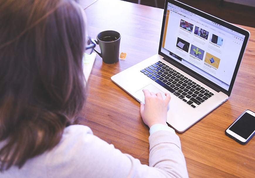 Woman working on laptop at wooden desk with coffee