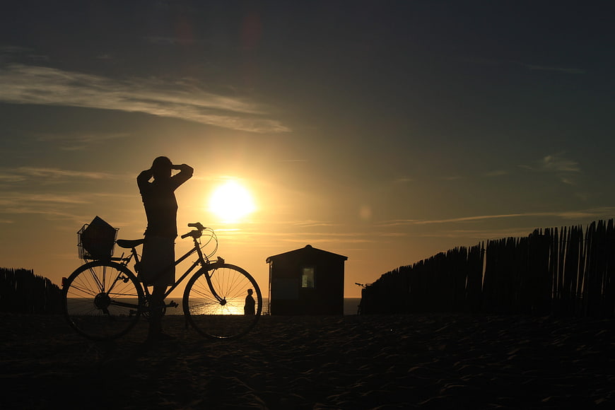 Silhouette of Cyclist with Bicycle on Beach at Sunset