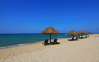 Tropical beach with thatched umbrellas and lounge chairs on sand