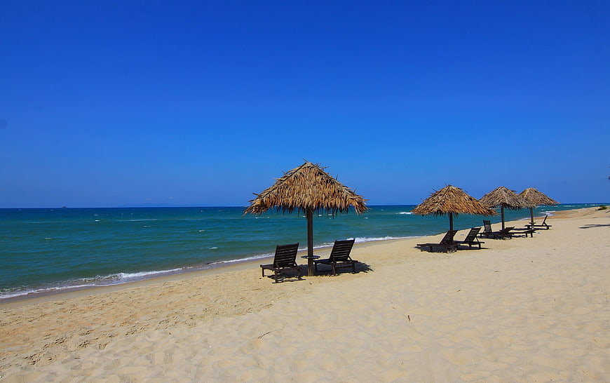 Tropical beach with thatched umbrellas and lounge chairs on sand