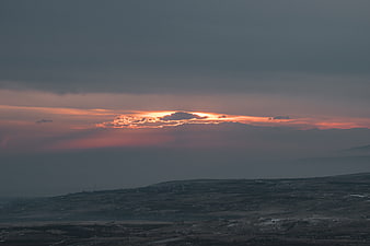 Dramatic sunset breaking through dark storm clouds over hilly landscape