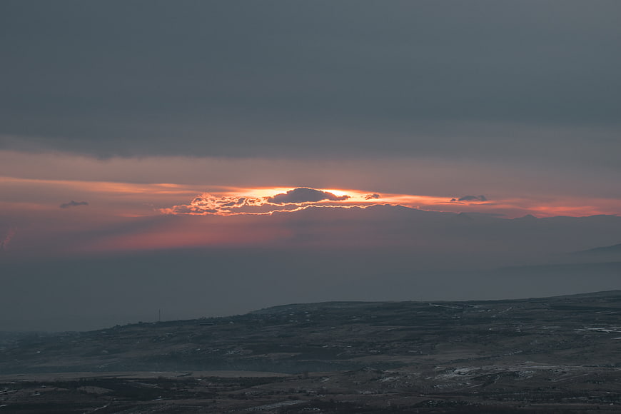 Dramatic sunset breaking through dark storm clouds over hilly landscape