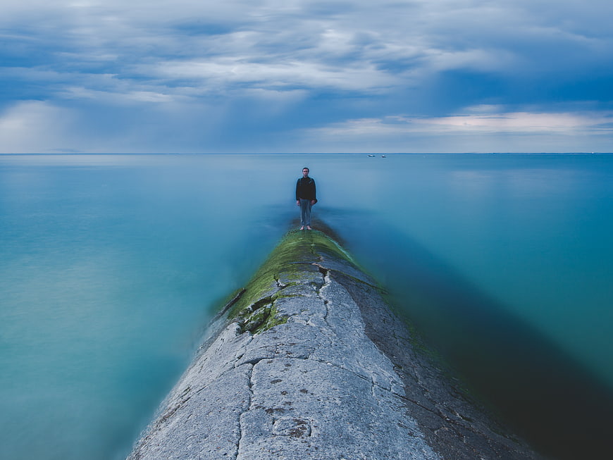 Man standing on mossy pier in calm blue ocean