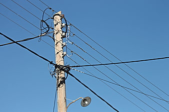 Wooden utility pole with tangled cables and street lamp against clear blue sky