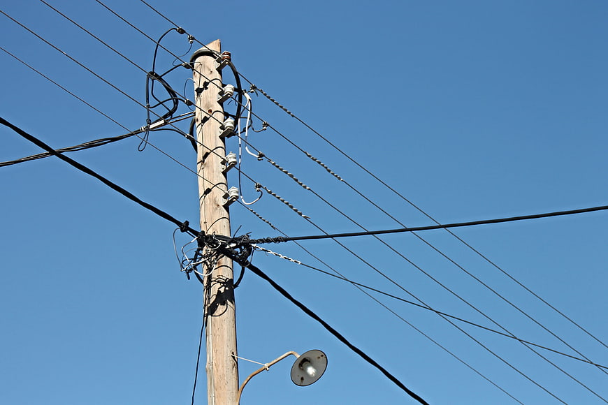 Wooden utility pole with tangled cables and street lamp against clear blue sky