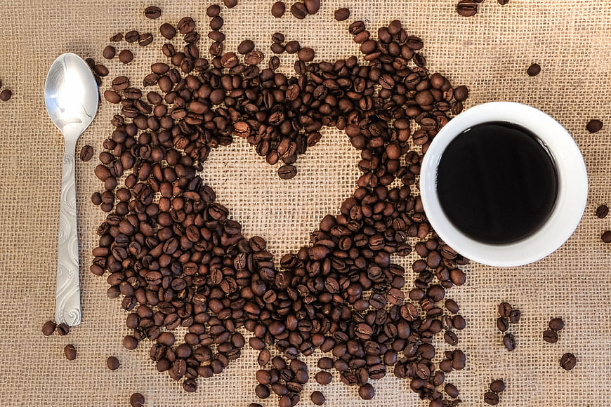 Coffee beans arranged in heart shape with cup of black coffee