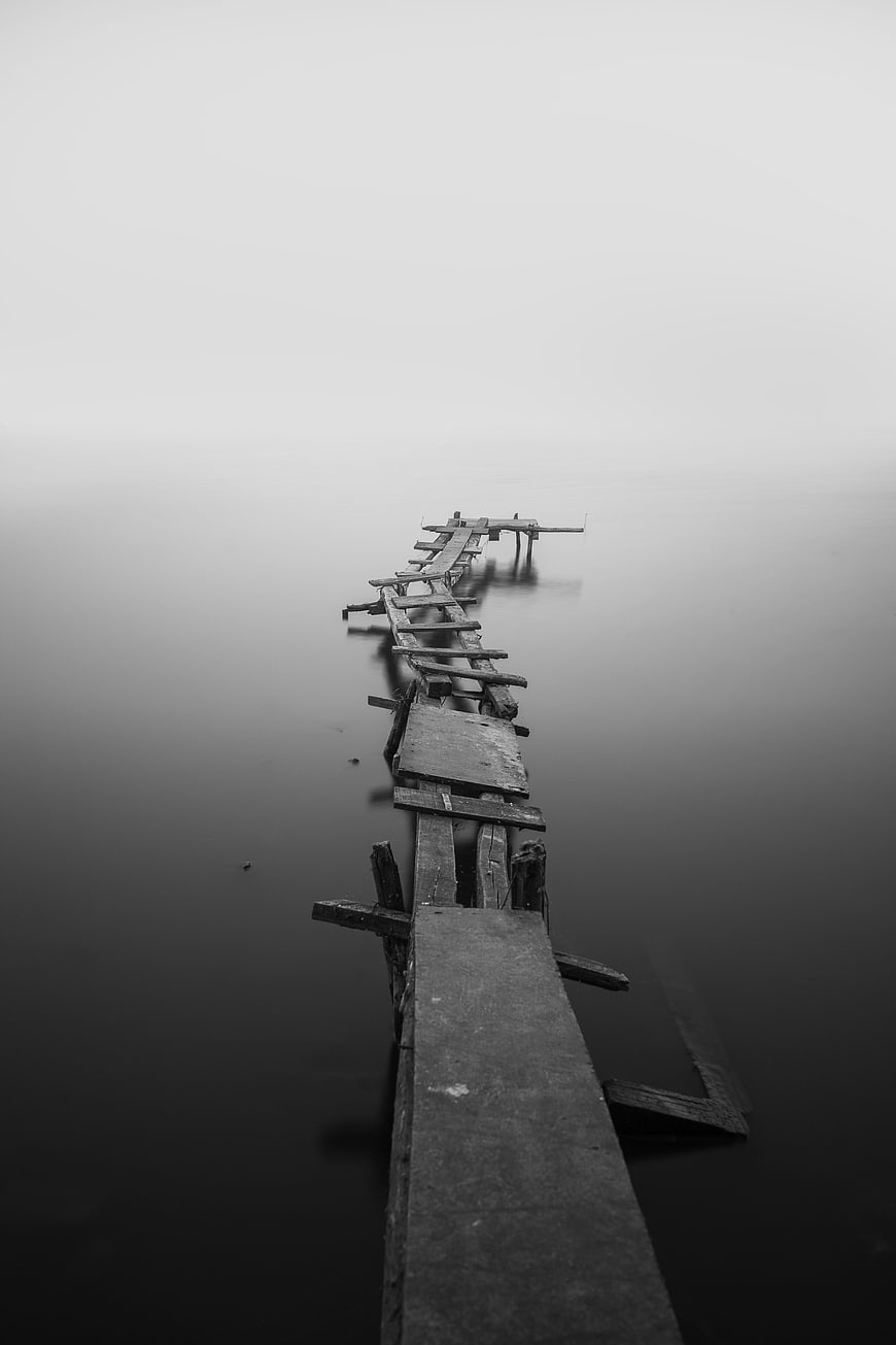 Decaying wooden pier extending into a foggy lake in black and white
