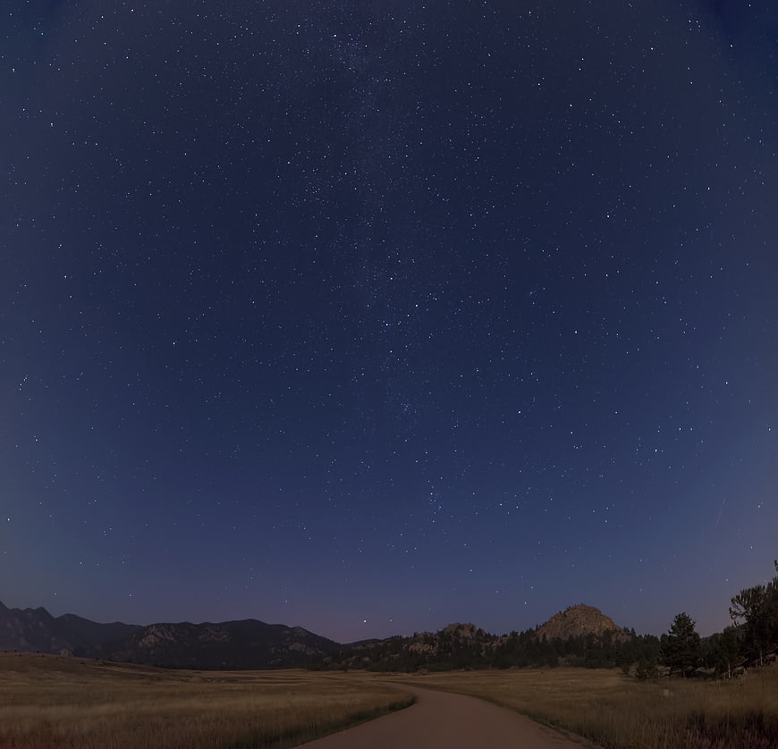 Starry Night Sky Over Mountain Road and Grassy Field