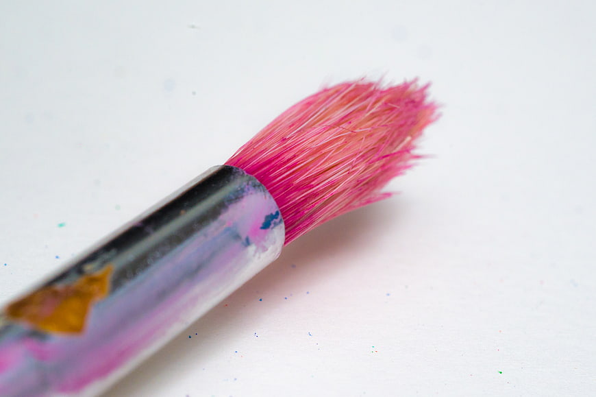 Close-up of pink paintbrush with colorful bristles on white background