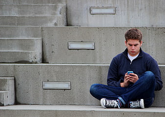 Teenager sitting on concrete steps texting on smartphone