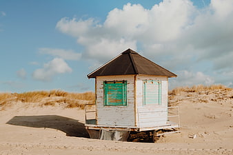 Weathered white beach hut with green shutters on sandy dunes