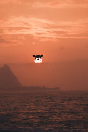 Drone Silhouette Flying Over Ocean at Sunset