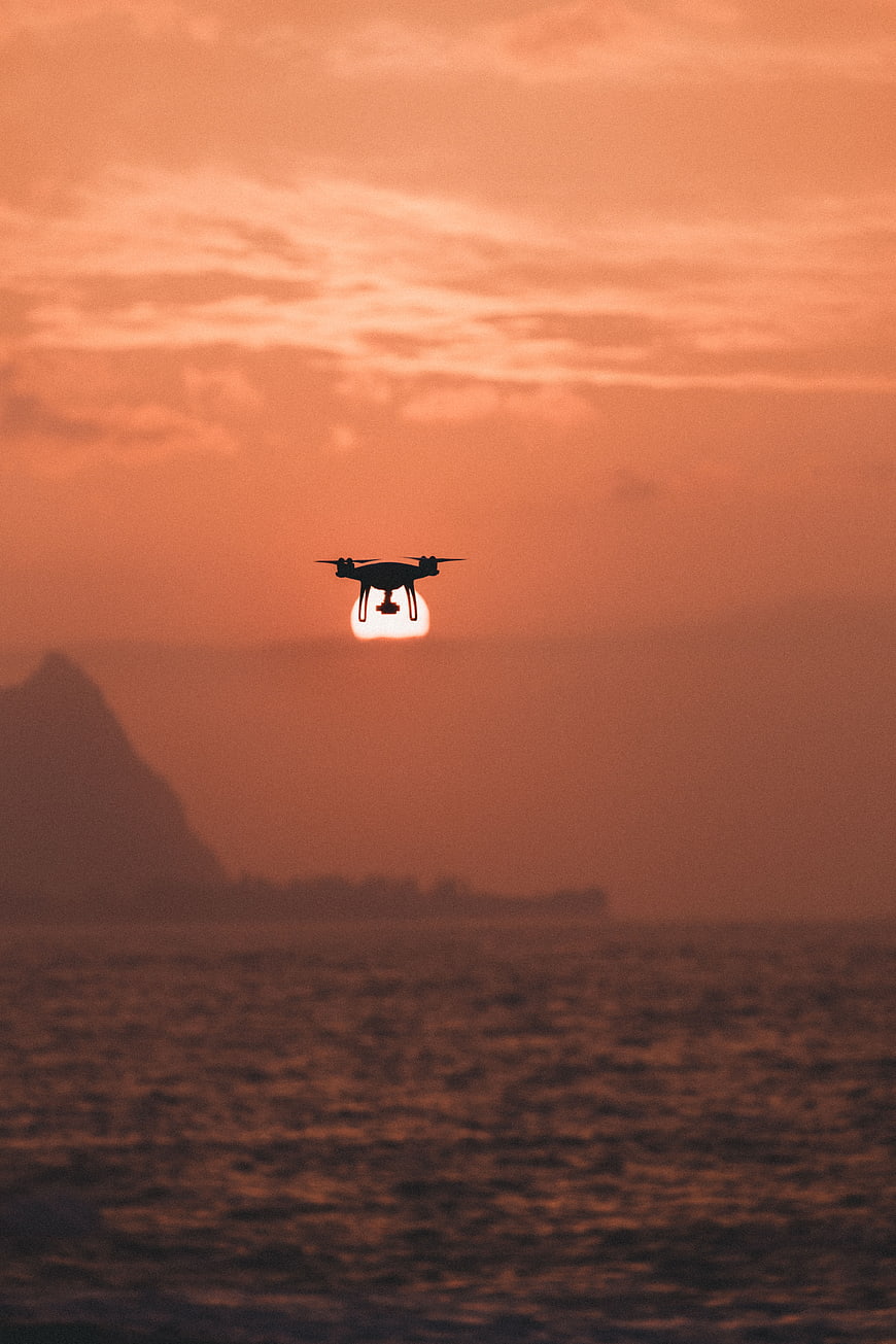 Drone Silhouette Flying Over Ocean at Sunset