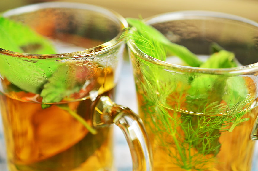 Close-up of two glass mugs filled with herbal tea and fresh green herbs