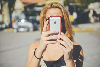 Young woman taking a photo with a red smartphone on a city street