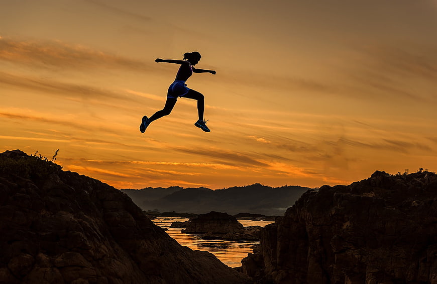 Silhouette of Woman Jumping Between Rocks at Sunset