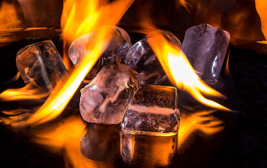 Ice cubes melting in fire flames on dark reflective surface