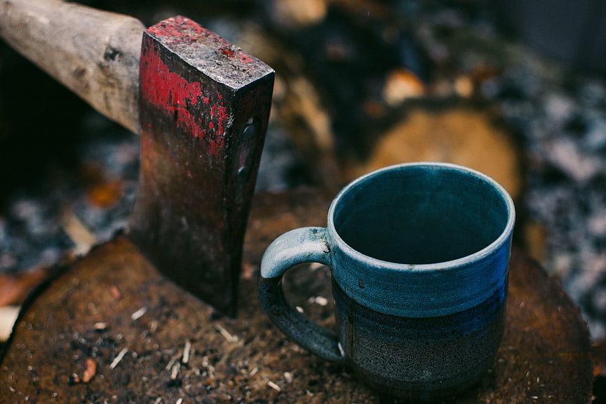 Rusty axe and blue ceramic mug on wood log