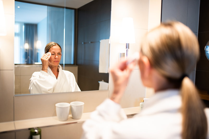 Woman applying skincare in bathroom mirror reflection