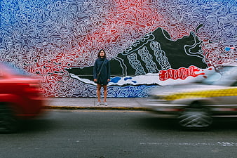 Woman standing before colorful street art mural with blurred traffic
